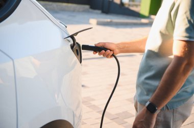 Erkek sürücünün şarj istasyonunda elektrikli aracını şarj ederken görüntüsü.