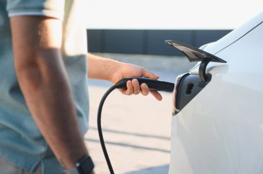 Dışarıdaki şarj istasyonunda şarj aletini elektrikli arabaya takan adama yaklaş.