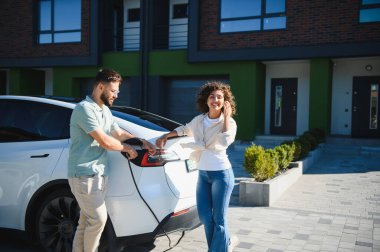 Evlerinde elektrikli araçlarını şarj eden mutlu çift, sürdürülebilir ulaşım ve yeşil enerji çözümlerini kucaklıyor