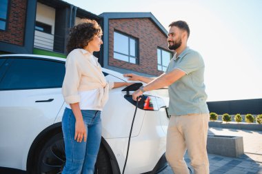 Mutlu ev sahipleri elektrikli araçlarını şarj ediyor, sürdürülebilir ve çevre dostu ulaşımın keyfini çıkarıyorlar