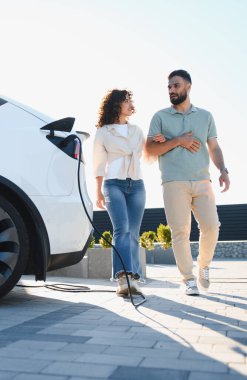 Genç çift evde elektrikli arabaları şarj olurken yürüyüş ve sohbetin tadını çıkarıyor, sürdürülebilir ve çevre dostu bir yaşam tarzı benimsiyorlar.