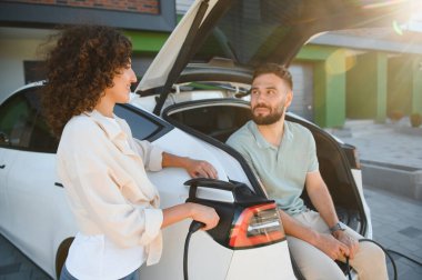 Genç çift elektrikli araçlarını evde şarj ediyor, sürdürülebilir ulaşım ve yenilenebilir enerji çözümlerini kucaklıyor