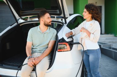 Genç çift elektrikli araçlarını evde şarj ediyor, çevre dostu ulaşım ve yenilenebilir enerji çözümlerine bağlılıklarını sergiliyorlar.