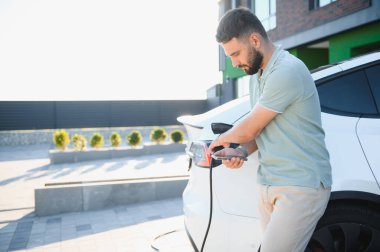 İşadamı şarj istasyonunda cep telefonu uygulamasını kullanarak elektrikli aracı şarj ediyor