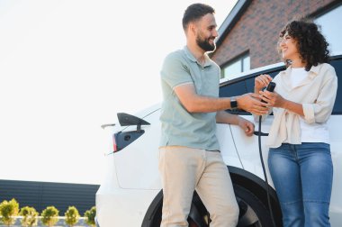 Mutlu çift elektrikli araçlarını evde şarj ediyor, çevre dostu ulaşım ve yenilenebilir enerji çözümlerine bağlılıklarını gösteriyor