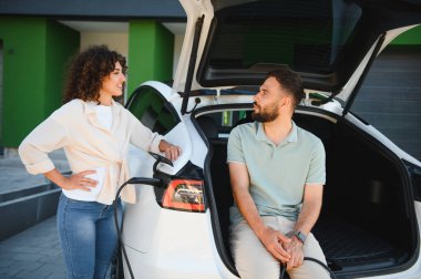 Mutlu çift elektrikli arabalarını evde şarj ediyor. Çevre dostu yaşam tarzına ve yenilenebilir enerjiye bağlılıklarını gösteriyor.