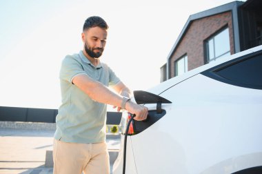 Genç adam öğleden sonra elektrikli arabasını şarj ediyor.