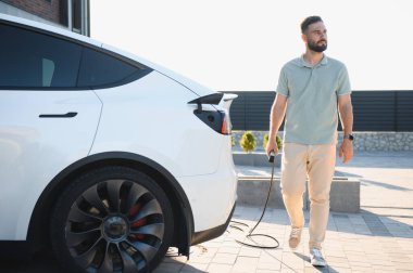Genç adam dışarıda elektrikli bir arabayı şarj ediyor.