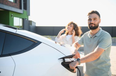 Mutlu çift elektrikli araçlarını evde şarj ediyor, çevre dostu ulaşım ve sürdürülebilir yaşam tarzlarına bağlılıklarını sergiliyorlar.