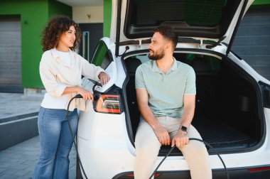 Genç çift elektrikli araçlarını evlerinde şarj ediyor, sürdürülebilir ve çevre dostu yaşam tarzı tercihleri sergiliyorlar.