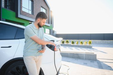 Adam akıllı telefon uygulaması kullanarak evinin önünde elektrikli araba şarj ediyor.