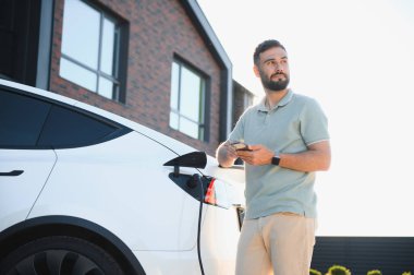 Adam evde elektrikli araç şarj ederken akıllı telefon kullanıyor.