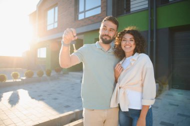 Heyecanlı ev sahipleri yeni evlerinin anahtarlarını gösteriyor, birlikte ilk mülklerini satın almalarını kutluyorlar, hayatlarında büyük bir dönüm noktası.