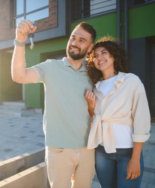 Gayrimenkul yatırımlarındaki başarılarını kutlamak için ellerinde yeni mülklerinin anahtarları olan genç bir çift.