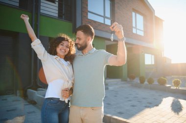 Mutlu çift yeni evlerinin anahtarlarını gösteriyor, başarılarını ve gayrimenkul yatırımlarını kutluyorlar.