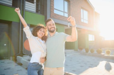 Yeni evlerinin anahtarlarını elinde tutan heyecanlı çift başarılı bir gayrimenkul alımının sevincini kutluyor ve geleceklerini birlikte kucaklıyorlar.