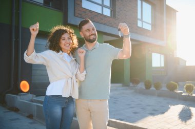 Heyecanlı çift yeni evlerinin anahtarlarını gösteriyor, sevinçle kollarını kaldırıyor ve başarılarını kutluyorlar.
