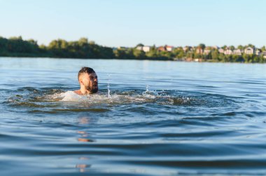 Sıcak bir yaz gününde nehir suyunda çırpınan sakallı bir adam nefes almak ve hayatta kalmak için mücadele ederken panik ve çaresizlik yaşıyor.
