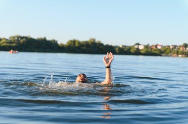 Adam gölde boğuluyor, çaresizce yardım için kolunu kaldırıyor, panik ve umutsuzluk anında suya karşı mücadele ediyor.