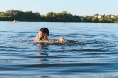 Güneşli bir yaz gününde neşeyle nehirde yüzen sakallı adam, suyun ferahlatıcı serinliğinin tadını çıkarıyor ve doğanın güzelliğini kucaklıyor.