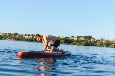 Genç adam, mavi gökyüzünün altında kıyıya yakın sakin bir göl gününün tadını çıkarırken güvenlik tasmasını çekiyor.