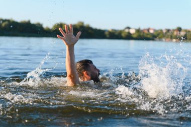 Gölde çırpınan sakallı bir adam, çaresizce yardım isterken dalgalara karşı savaşıyor, korku ve çaresizliği somutlaştırıyor.
