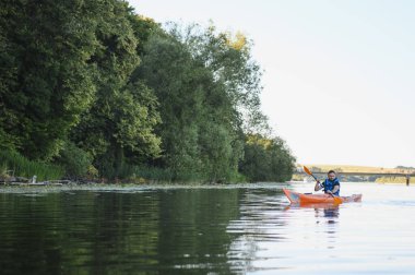Kanocu, yemyeşil ormanlarla çevrili sakin bir nehirde huzurlu bir kürek çekerek doğada huzurlu bir an sergiliyor.