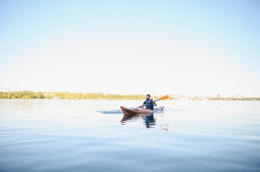 Huzurlu bir gölde kayak yapan bir adam, su sporlarının tadını çıkaran ve doğanın güzelliği arasında aktif bir eğlence arayan bir adam.
