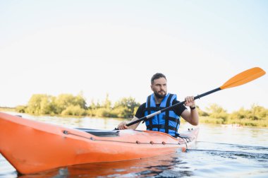Parlak turuncu bir can yeleği giyen, yazın sakin bir nehirde kano süren, aktif su dinlenme ve maceranın keyfini kucaklayan bir adam.