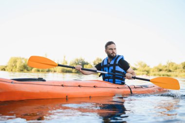 Gölde veya nehirde turuncu kano süren, can yeleği giyen, su sporlarının ve aktif eğlencelerin tadını çıkaran bir adam.
