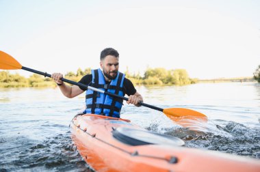 Yazın nehirde turuncu kano süren bir adam can yeleği giyiyor, aktif eğlence ve su sporlarının tadını çıkarıyor.