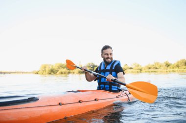 Can yeleği giyen bir adam yaz boyunca nehirde kano yapıyor, su sporlarının heyecanını yaşıyor ve aktif olarak dinleniyor.