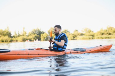 Can yeleği giyen adam gölde turuncu kano sürüyor, su sporlarının ve yazın aktif dinlenmenin tadını çıkarıyor.