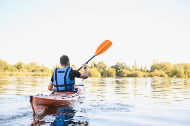 Huzurlu gölde kano süren bir adam, doğanın huzurunun tadını çıkarıyor ve aktif olarak dinleniyor.