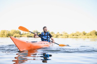 Adam dingin bir gölde kanoyla kürek çekiyor, su sporlarının tadını çıkarıyor ve güneşli bir yaz gününde doğanın güzelliğini kucaklıyor.