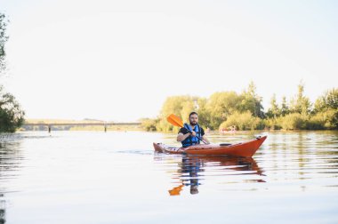 Sakin bir nehirde kayak yapan bir adam, sıcak yaz havasının tadını çıkarırken aktif bir eğlence ve doğanın güzelliğinin tadını çıkarıyor.