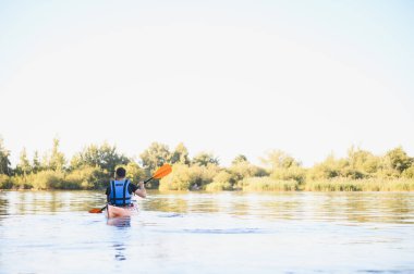 Bereketli yeşilliklerle çevrili sakin bir göl boyunca kano kürek çeker. Huzurlu bir su sporları macerası sırasında doğanın huzurunun tadını çıkarır.