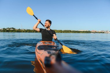 Parlak güneşin altında bir nehirde kürek çeken kanocu, su sporlarının heyecanını kucaklıyor ve aktif bir açık hava yaşam tarzının tadını çıkarıyor.