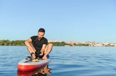 Genç sporcu yemek masasında oturmuş, sakin bir gölün sakin sularında kürek çekmeye hazırlanırken tasmasını ayarlıyor.