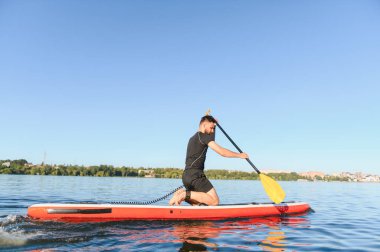 Genç sporcu bir yemek masasında kürek çekiyor. Gölde güneşli bir günün tadını çıkarıyor. Aktif olarak dinleniyor.