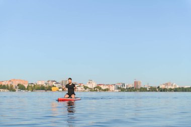 Suyun sakin bir zemininde, arka planda şehir manzarası olan ve aktif eğlence ve su sporları sunan bir adam ustaca kürek çekiyor.