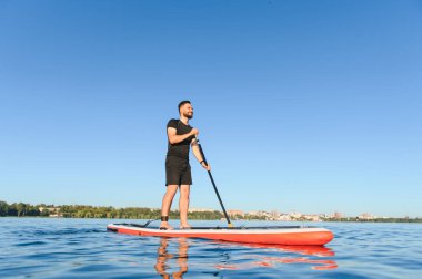Durgun bir gölde kürek çeken bir adam, açık deniz sporları ve macera dolu güneşli bir günün tadını çıkarıyor.