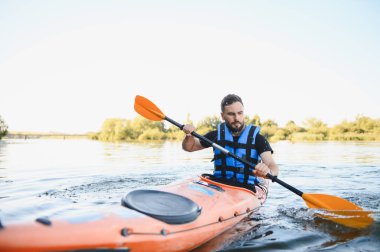 Güzel bir yaz gününde nehirde kano süren bir adam, aktif dinlenme ve su sporlarının tadını çıkarıyor.