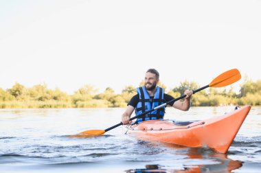Huzurlu bir nehirde kano süren bir adam, doğanın huzurunun tadını çıkarırken aktif bir eğlence ve yaz güneşinin tadını çıkarıyor.