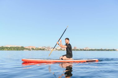 Genç sporcu, bir gölün üstünde ayakta duran bir kürek çekerken şehirde su sporlarının keyfini çıkarıyor.
