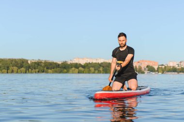 Genç sporcu, şehirdeki bir gölde, su sporlarının ve aktif eğlencelerin tadını çıkaran bir panoda kürek çekiyor.
