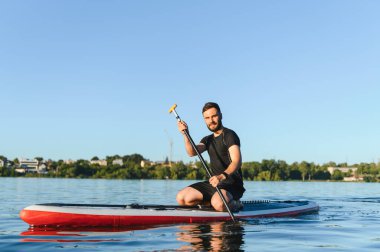 Genç sporcu, yemek masasında diz çökerken, gölde güneşli bir yaz gününün tadını çıkarıyor.