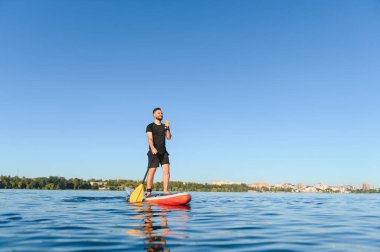 Genç sporcu yazın göl kenarındaki yemek masasında kürek çekiyor, su sporunun ve güneşli havanın tadını çıkarıyor.