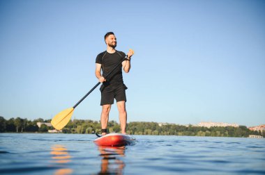 Genç sporcu yemek masasında kürek çekiyor, güneşli bir günde gölün sessizliğinin tadını çıkarıyor, aktif olarak dinleniyor.