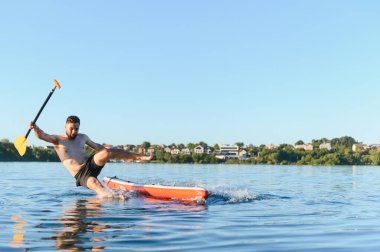 Genç adam dengesini kaybediyor ve yaz tatili sırasında yemek masasından göle düşüyor, elinde kürekle havada.